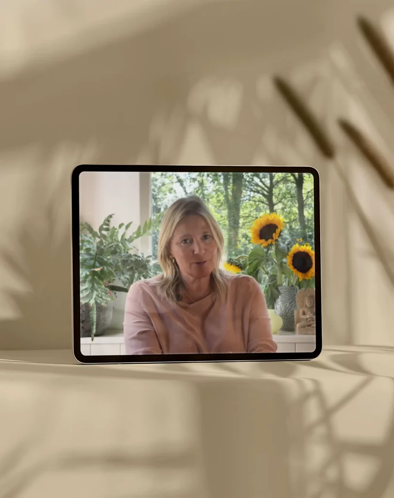 Tablet met videoles van coach Ingrid uit de cursus Hart voor Jezelf, gefilmd bij een raam met zonnebloemen en planten op de achtergrond.